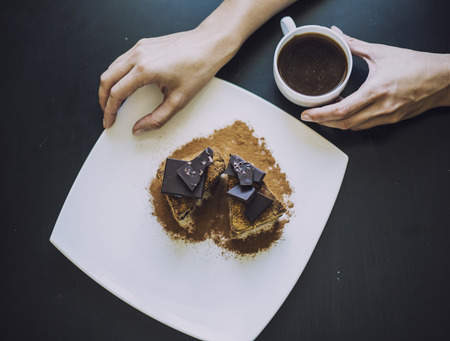 Female hand with a Cup of coffee and a beautiful chocolate cake closeup on the tableの写真素材