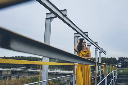 Beautiful young happy girl is walking along the railing of a construction in a bright dressの写真素材