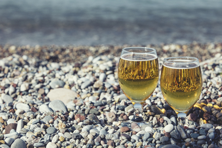 Two beautiful glass with light refreshments on the pebbles on the sea shoreの写真素材
