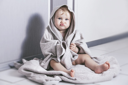 Little baby sitting in the tub wrapped a big towelの写真素材