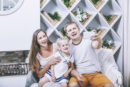 Happy beautiful young family father, mother and daughter are doing selfie on mobile smile together at homeの写真素材