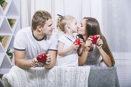 Happy beautiful young family father, mother and daughter with red hearts smiling together at homeの写真素材