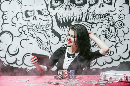 Beautiful young woman with a successful gambling tablet, online casino at a table with cards, chipsの写真素材