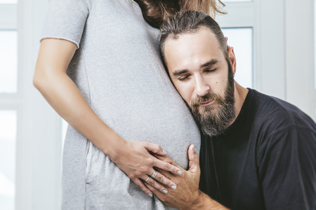 Heterosexual couple beautiful young man and a pregnant woman on a background of white windowの写真素材