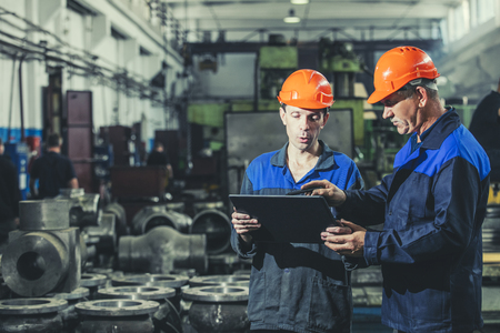 Two workers at an industrial plant with a tablet in hand, working together manufacturing activitiesの写真素材