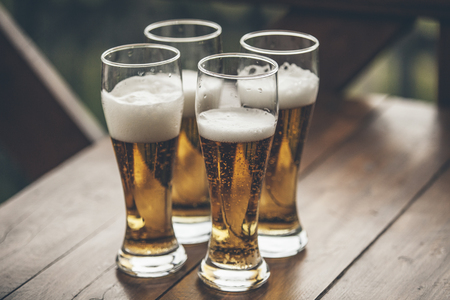 Beer with foam light tall boys standing on a wooden table closeupの写真素材