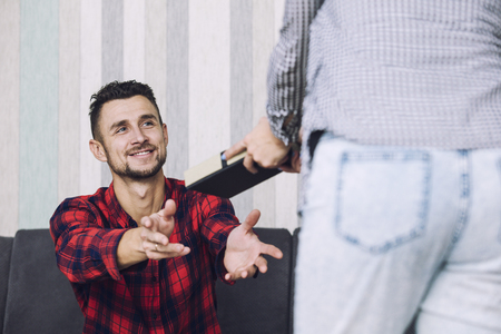 Happy beautiful couple, a woman gives a man a gift for the holiday at home togetherの写真素材