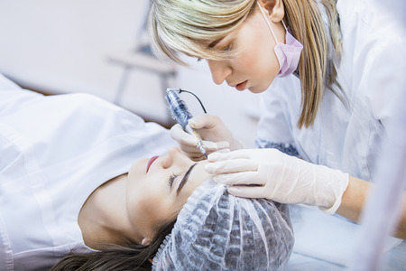 Beautician female applies permanent makeup on eyebrows, tattoo eyebrows on beautiful models in a beauty parlorの写真素材