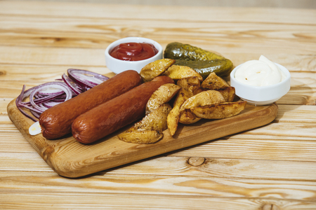 Sausages with baked potatoes sauces, onions and pickles on a wooden Board on the tableの写真素材