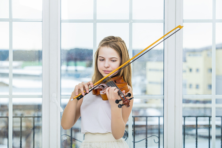 Child girl playing the violin to study beautiful and happy in a white room with a large windowの写真素材