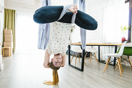Young woman doing yoga in the air on a swing at homeの写真素材