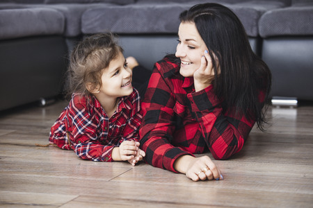 Beautiful happy family mother and daughter smiling together at home lying on the wooden floor in the living roomの写真素材