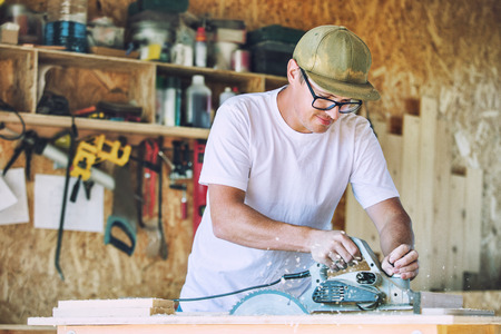 Adult young man working in a carpenter's shop working with tools on the productの写真素材