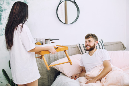 Young beautiful and happy couple man and woman at home in bedroom with bed having Breakfast romantic