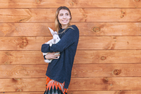 Young beautiful woman with a white rabbit in her arms next to a wooden house in the countrysideの写真素材