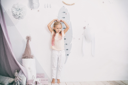 Little beautiful child girl in the children's playroom measures her heightの写真素材