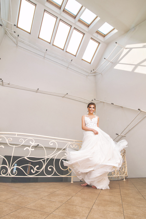 Luxurious young beautiful happy bride in a fashionable wedding dress in a big white roomの写真素材