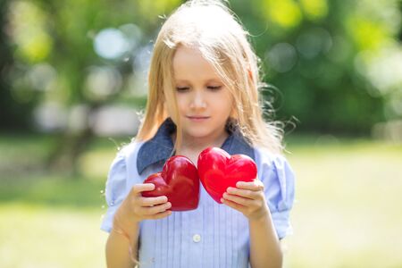 Small and beautiful girl child sweet and happy with two red hearts in her handsの写真素材