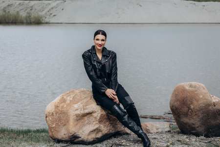 Model, a beautiful brunette woman in a black leather jacket, portrait on a stone by a pondの写真素材