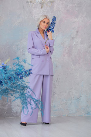 Young beautiful girl model blonde with hair and makeup in a fashionable violet color suit and with flowersの写真素材