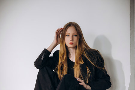 Beautiful blonde model, young girl, teenager in the studio in a black jacket on a white cyclorama