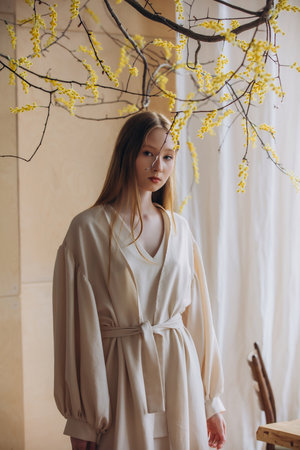 Beautiful blonde model, young girl, teen in studio in beige dress with mimosa flowersの写真素材