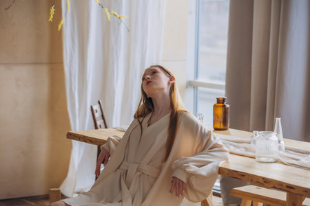 Beautiful blonde model, young girl, teenager in the studio in a beige dress in the interior with a tableの写真素材