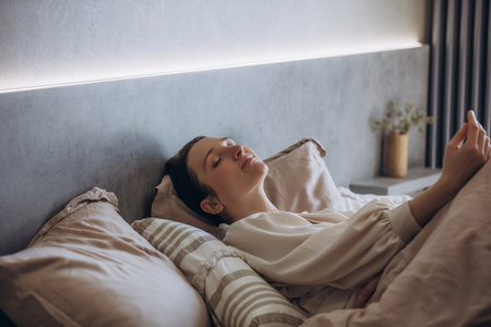 A beautiful brunette woman is resting on a bed in the bedroomの写真素材