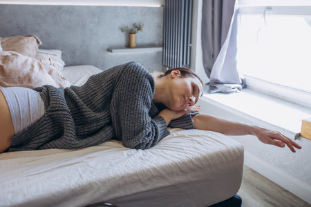 A beautiful brunette woman in the bedroom on the bed and wearing a sweaterの写真素材