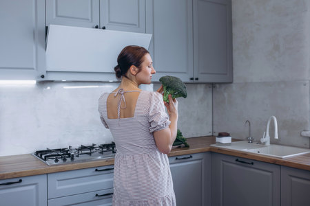 A beautiful brunette woman in the kitchen with green broccoli in her handsの写真素材