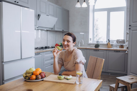 A beautiful brunette woman in the kitchen with a green apple and fruitsの写真素材