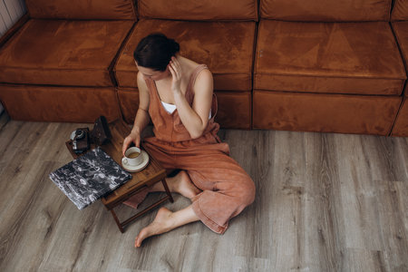 A beautiful brunette woman in a room on the floor by the sofa with a camera, hobbies, creativityの写真素材