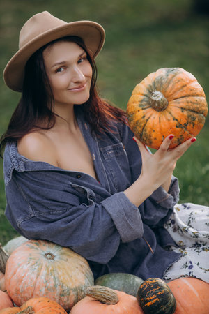 Woman is a young adult brunette in a straw hat with a pumpkin harvestの写真素材