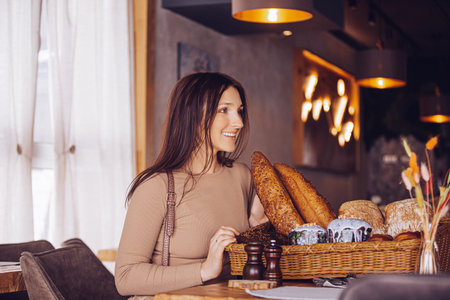 Young adult brunette woman is sitting at a table with a lot of fresh pastries.の写真素材