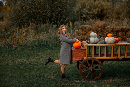 Blonde model girl in a coat on the background of a pumpkin cartの写真素材