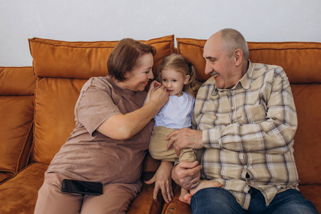 Grandmother and grandfather with their baby granddaughter sitting on the couch at home togetherの写真素材