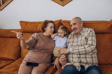 Grandmother and grandfather with their baby granddaughter sitting on the couch at home togetherの写真素材