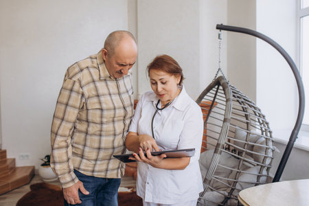 Female doctor with tablet gives treatment recommendations to elderly pensioner manの写真素材