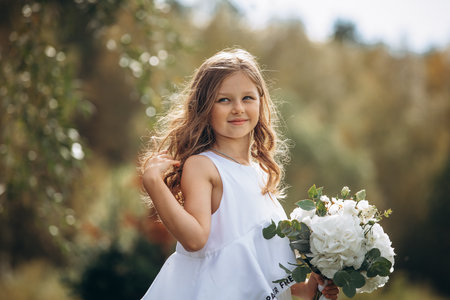 Beautiful girl child with a white dress with a bouquet of flowers, portrait in natureの写真素材