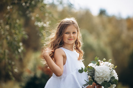 Beautiful girl child with a white dress with a bouquet of flowers, portrait in natureの写真素材