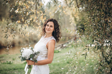 Beautiful young woman in a white dress with a bouquet in her hands in nature, portraitの写真素材