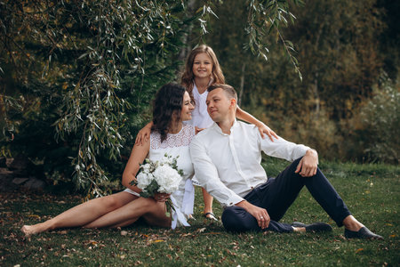 Family mother, father and daughter are beautiful and happy together on a holiday, in white clothes and with a bouquet, in natureの写真素材
