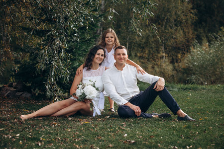 Family mother, father and daughter are beautiful and happy together on a holiday, in white clothes and with a bouquet, in natureの写真素材