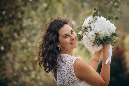 Beautiful young woman in a white dress with a bouquet in her hands in nature, portraitの写真素材