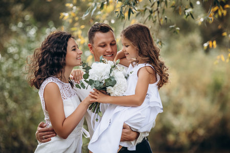 Family mother, father and daughter are beautiful and happy together on a holiday, in white clothes and with a bouquet, in natureの写真素材