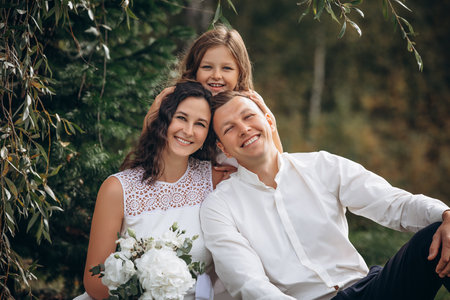 Family mother, father and daughter are beautiful and happy together on a holiday, in white clothes and with a bouquet, in natureの写真素材