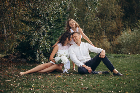 Family mother, father and daughter are beautiful and happy together on a holiday, in white clothes and with a bouquet, in natureの写真素材