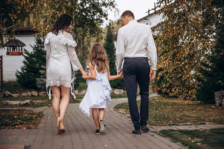 Family mother, father and daughter are beautiful and happy together, in white clothes, on a walkの写真素材