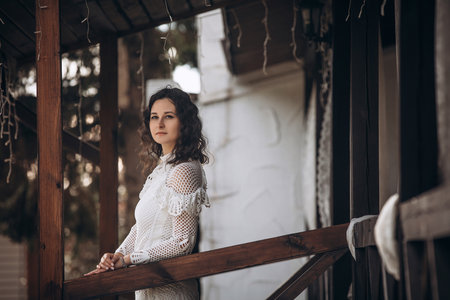 Beautiful young brunette woman in a white dress on the veranda of the houseの写真素材