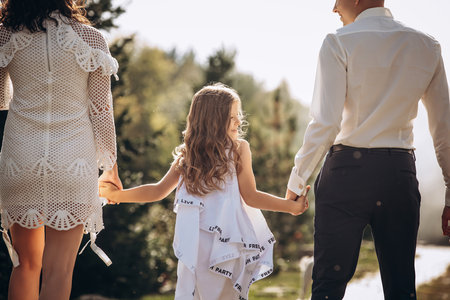 Family mother, father and daughter are happy together, in white clothes, on a walkの写真素材